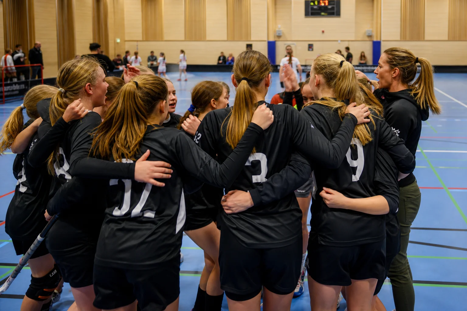 Tjejlag i innebandyhuddle efter match, händer på axlar